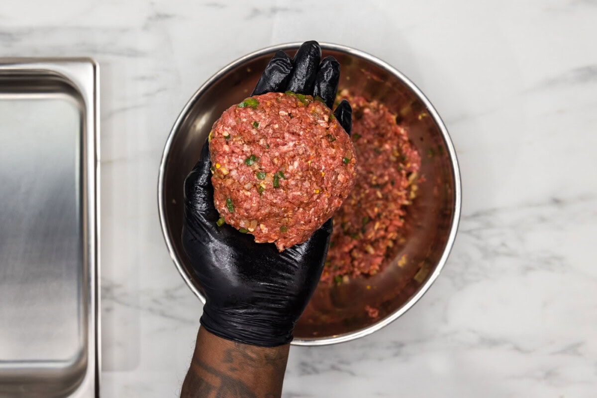 gloved hand holding burger patty