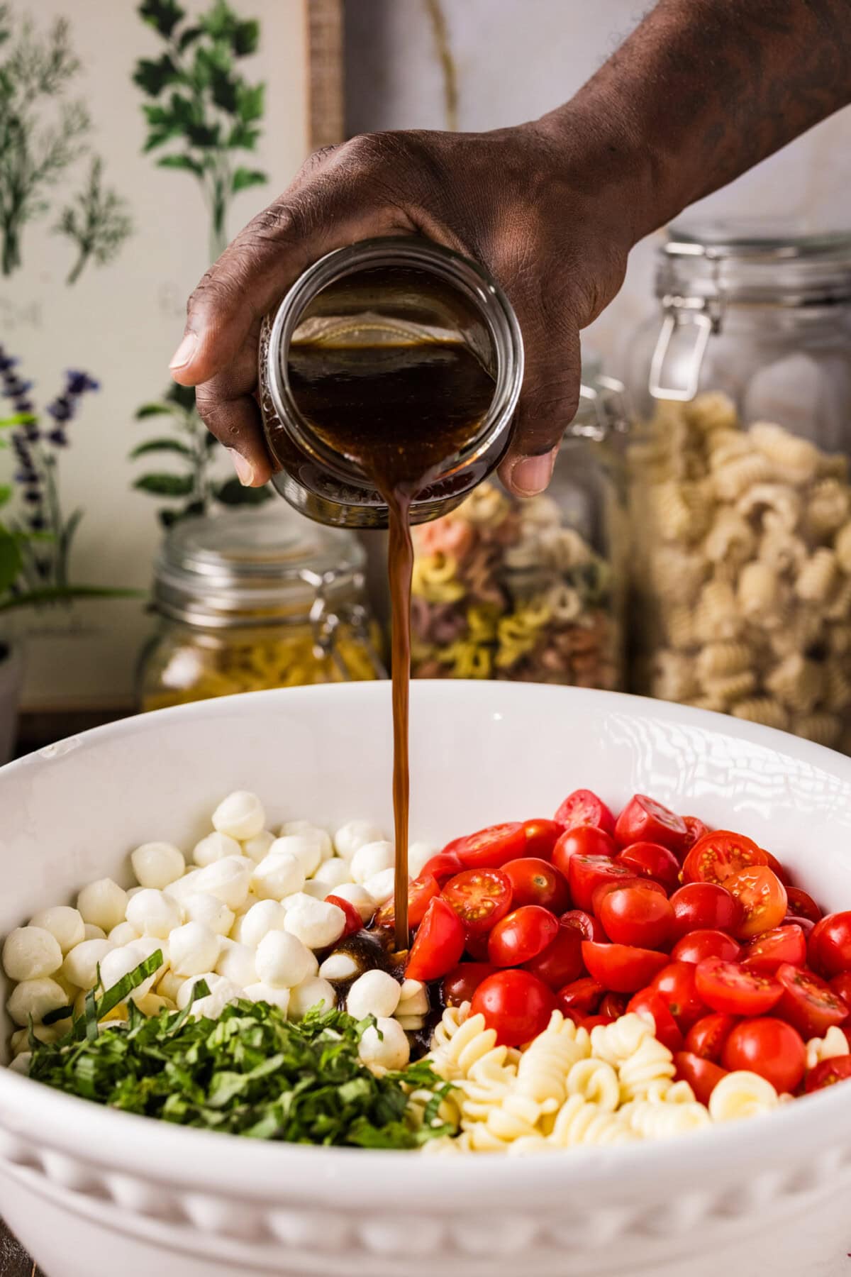 pouring balsamic vinaigrette over caprese pasta salad in a bowl