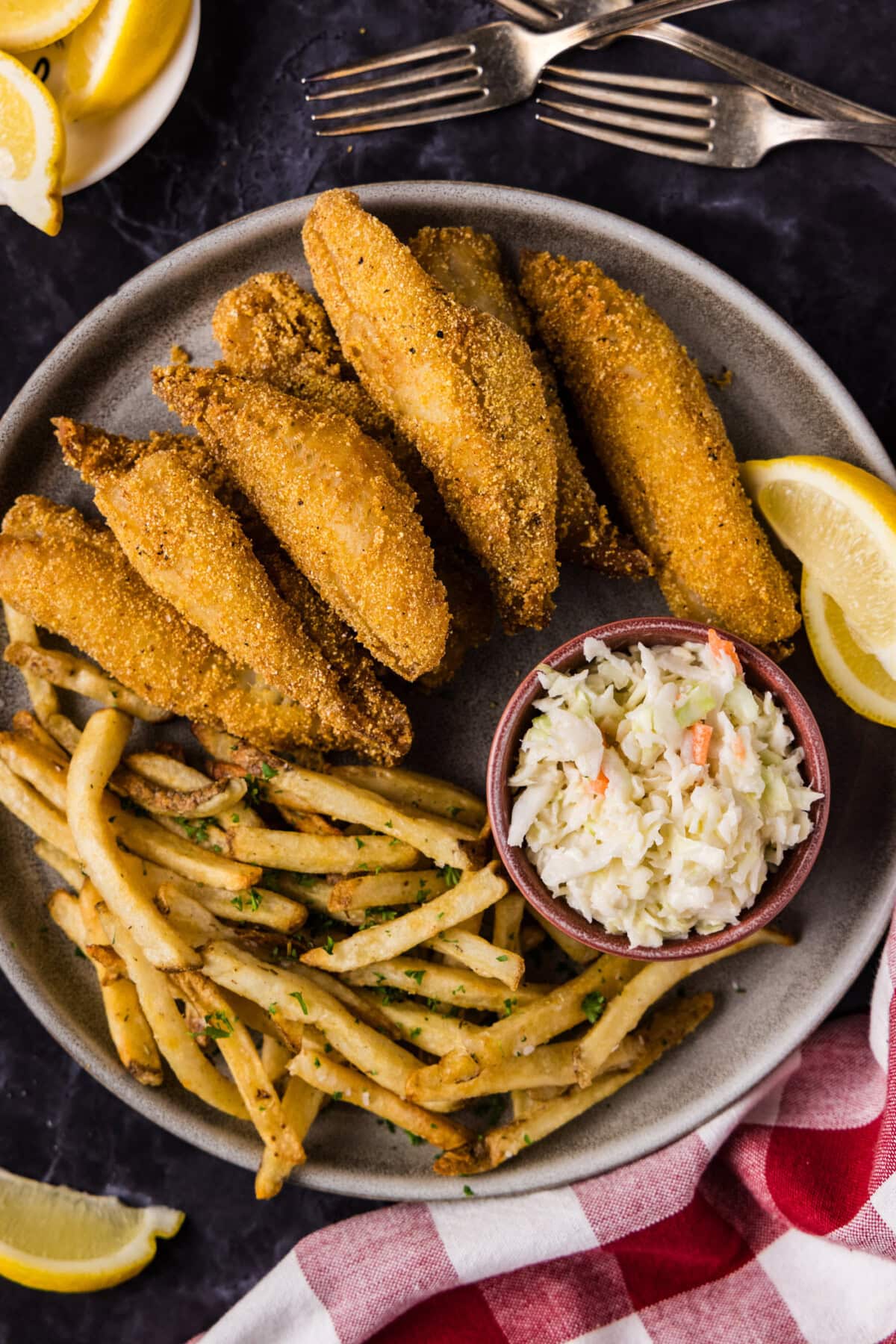 Close up photo of Fried Perch on a plate with fries, coleslaw and lemon wedges on the side