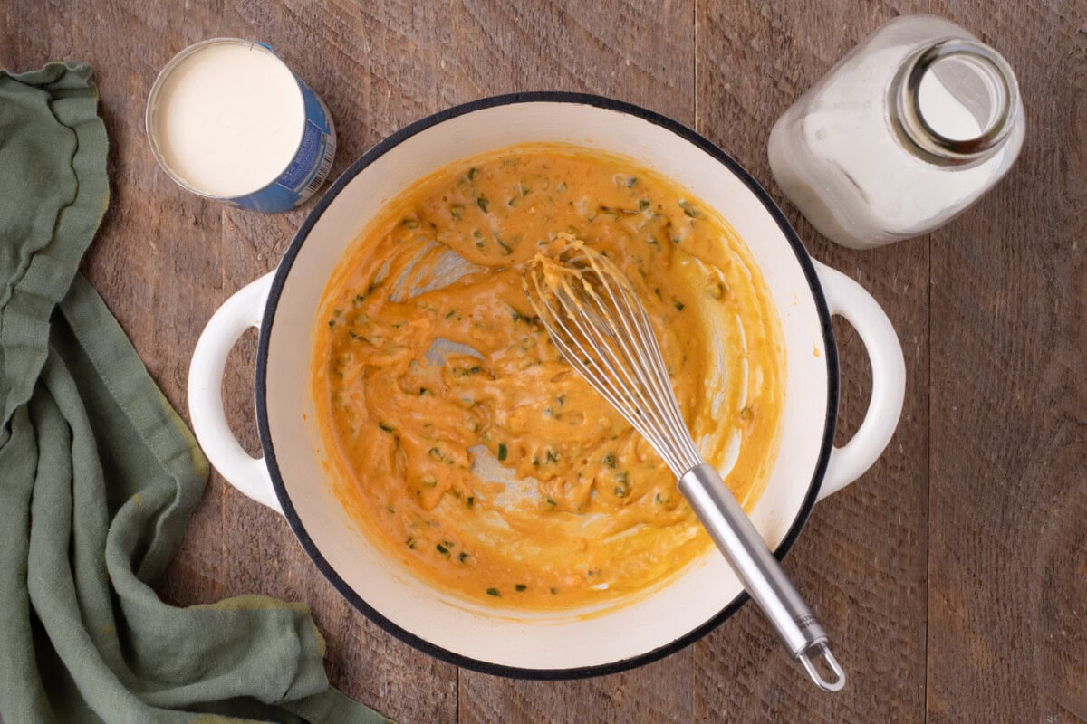 whisking evaporated milk into jalapeno mixture in a pot
