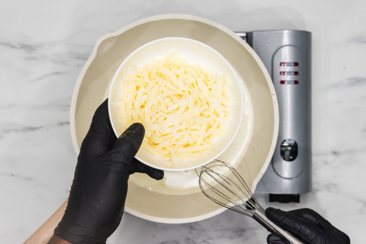 hand holding cheese over a skillet of heavy cream