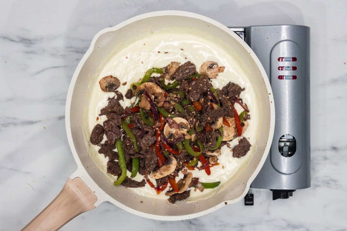 steak and veggie mixture added to skillet of heavy cream and cheese sauce