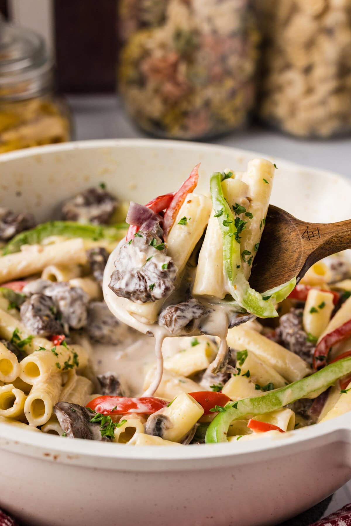 Spoonful of Philly Cheesesteak Pasta held above a skillet of Philly Cheesesteak Pasta