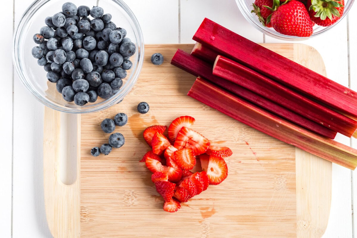 Bowl of blueberries, rhubarb and chopped strawberries on a wooden cutting board