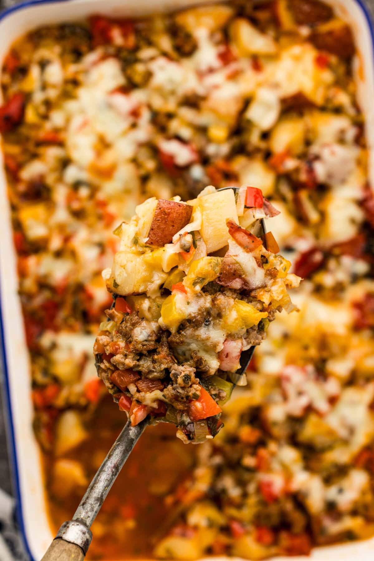 Spoonful of Sausage and Potato Casserole held above a casserole dish