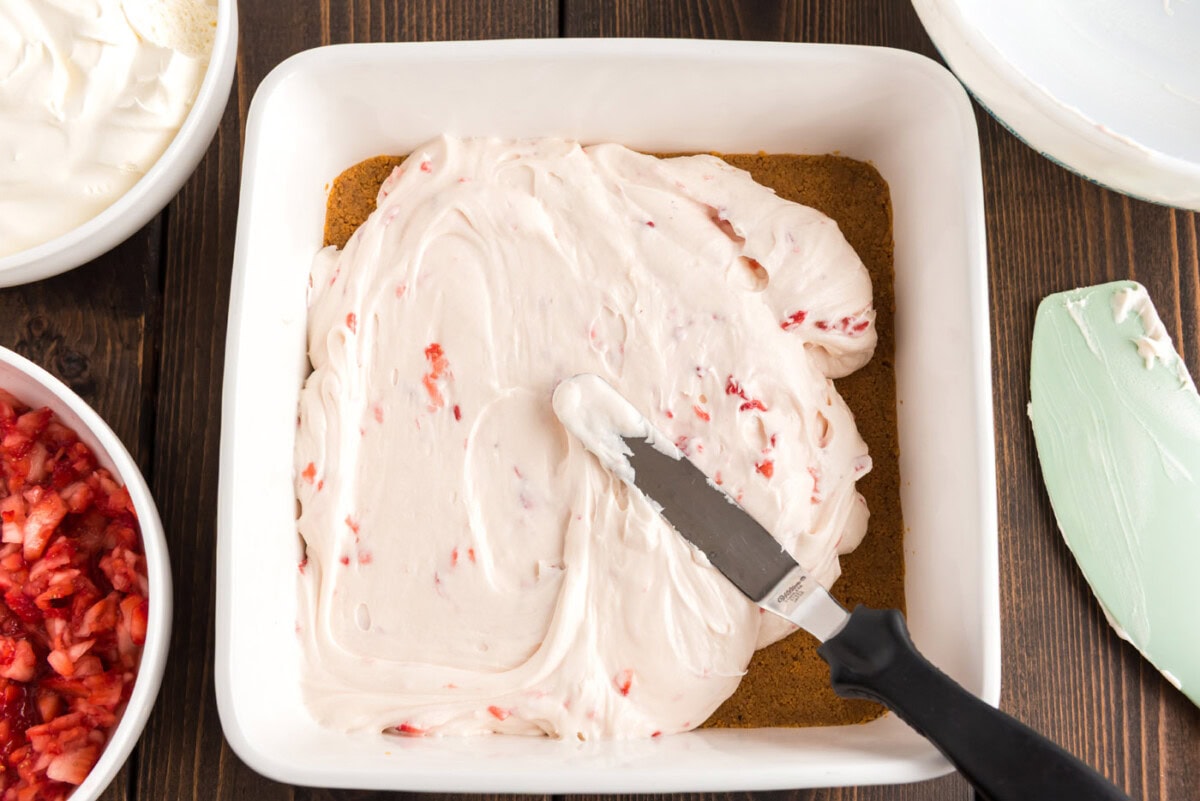spreading strawberry cream cheese filling over graham crust