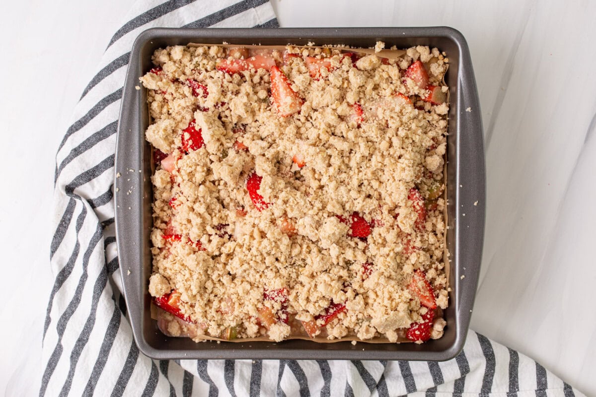 crumble topping over strawberry rhubarb crumble bars in a pan