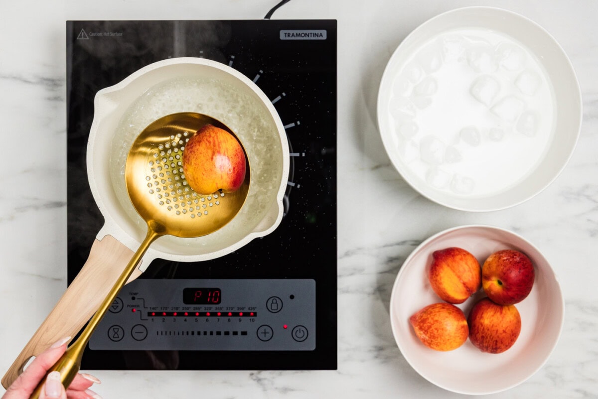 slotted spoon holding peaches over boiling water