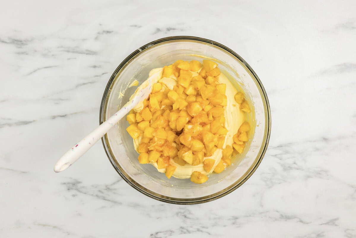 rubber spatula in a bowl with chopped peaches and cake batter