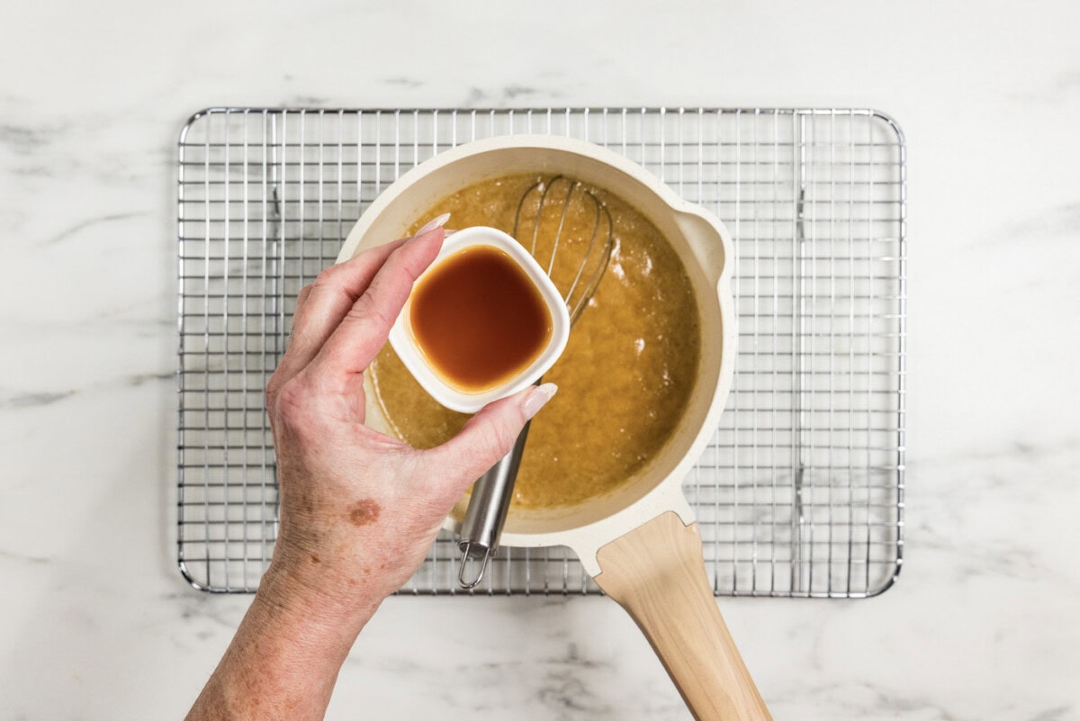 hand holding vanilla over caramel mixture in a saucepan