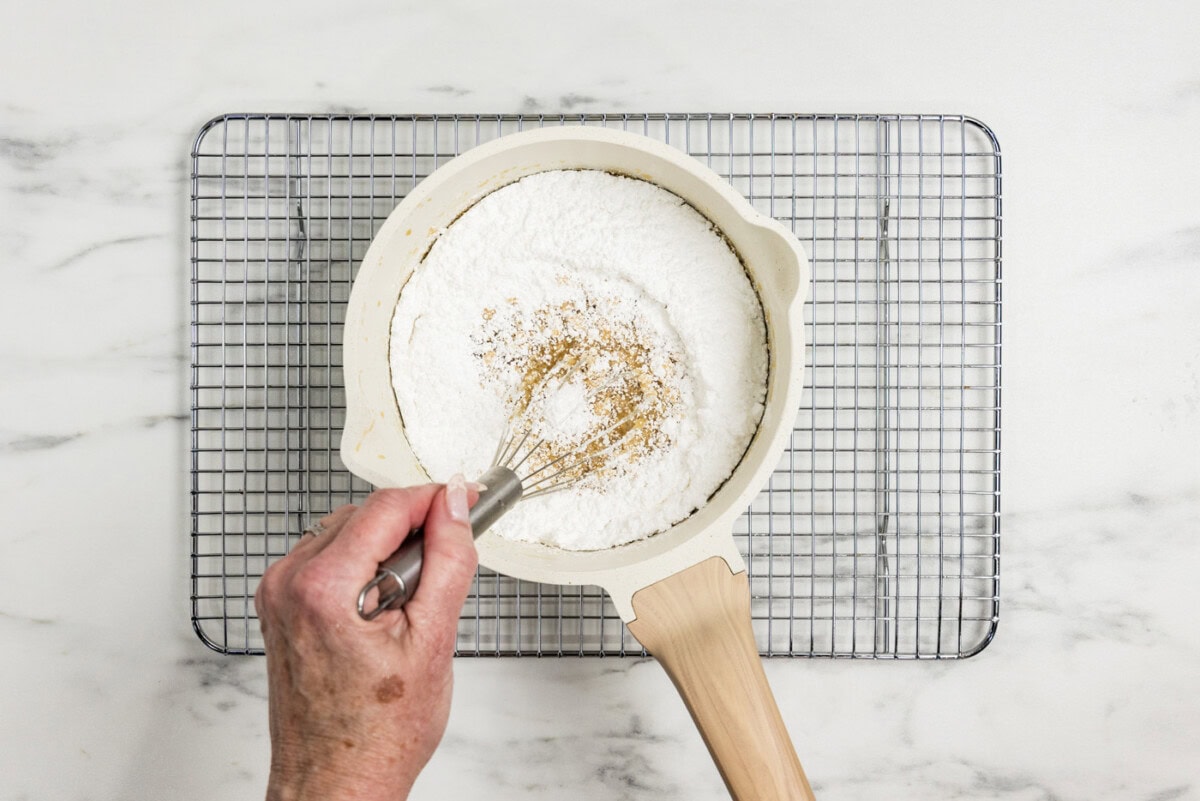whisking powdered sugar in a saucepan of caramel icing