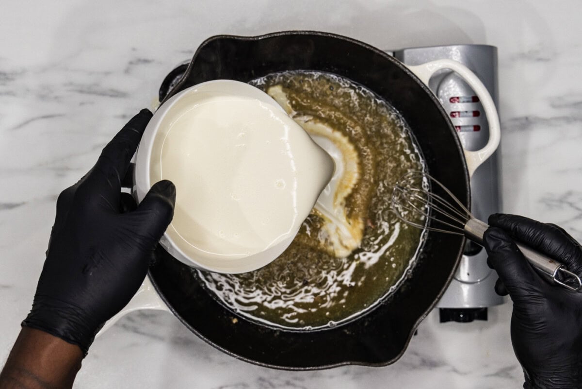 pouring heavy cream into skillet with broth