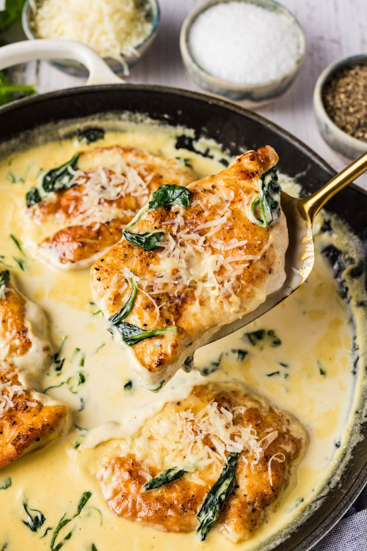 Spatula holding up a piece of Chicken Florentine above a skillet