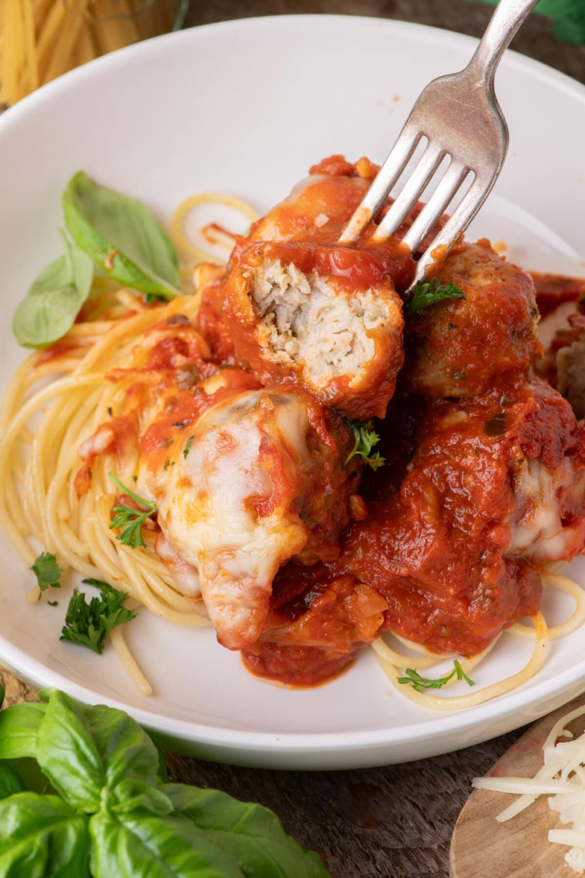 Fork holding half of a Chicken Parmesan Meatball over spaghetti and meatballs