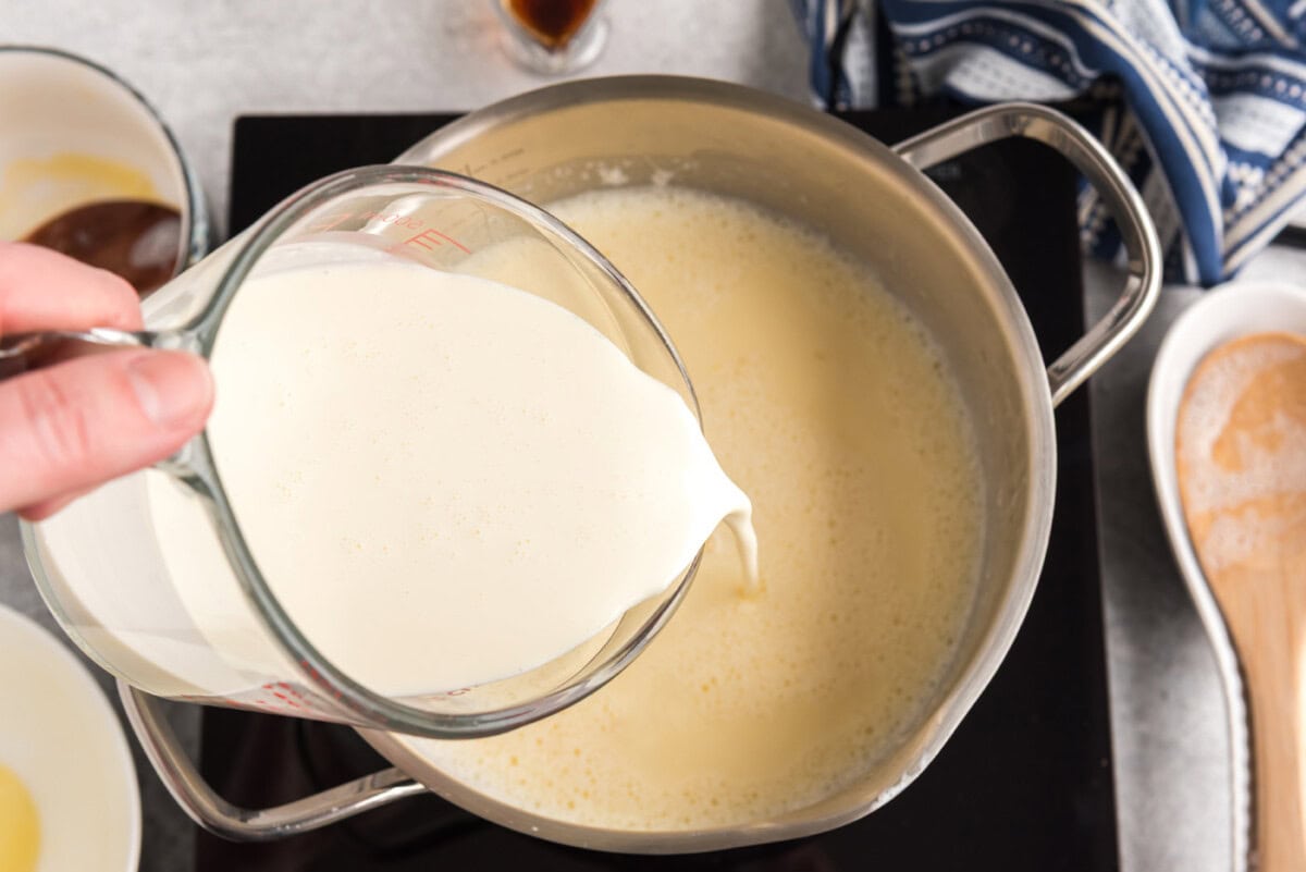 pouring heavy cream into saucepan of egg and milk mixture