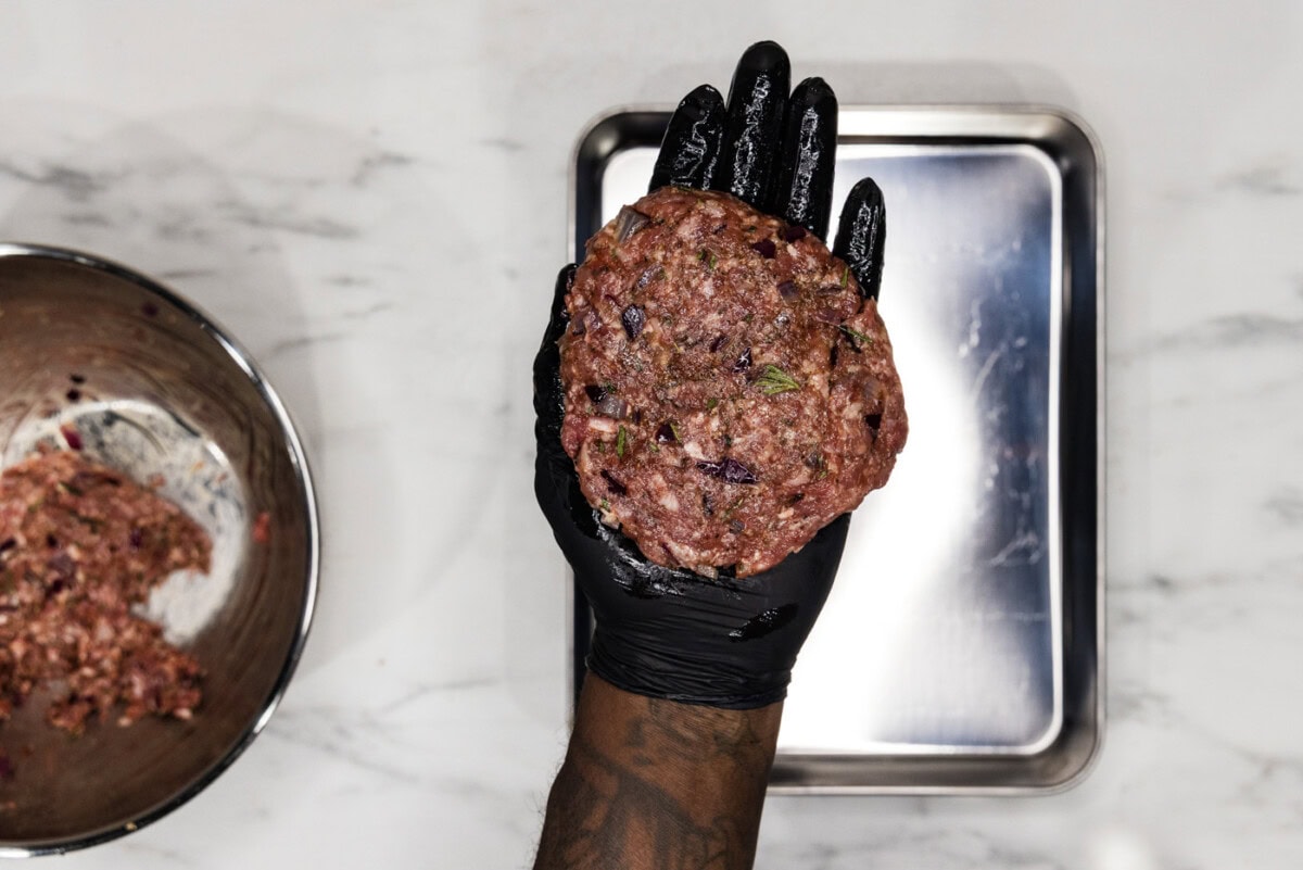 gloved hand holding a lamb burger patty