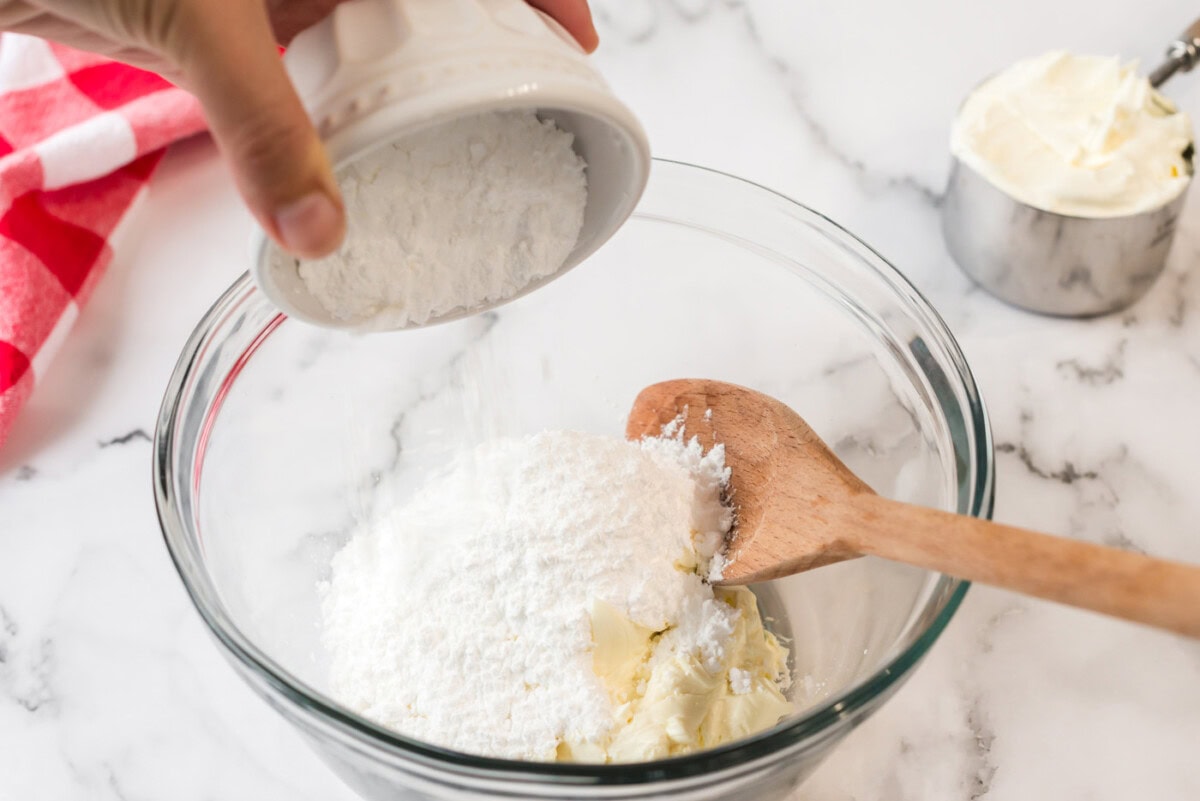 Powdered sugar being added to a bowl of cream cheese
