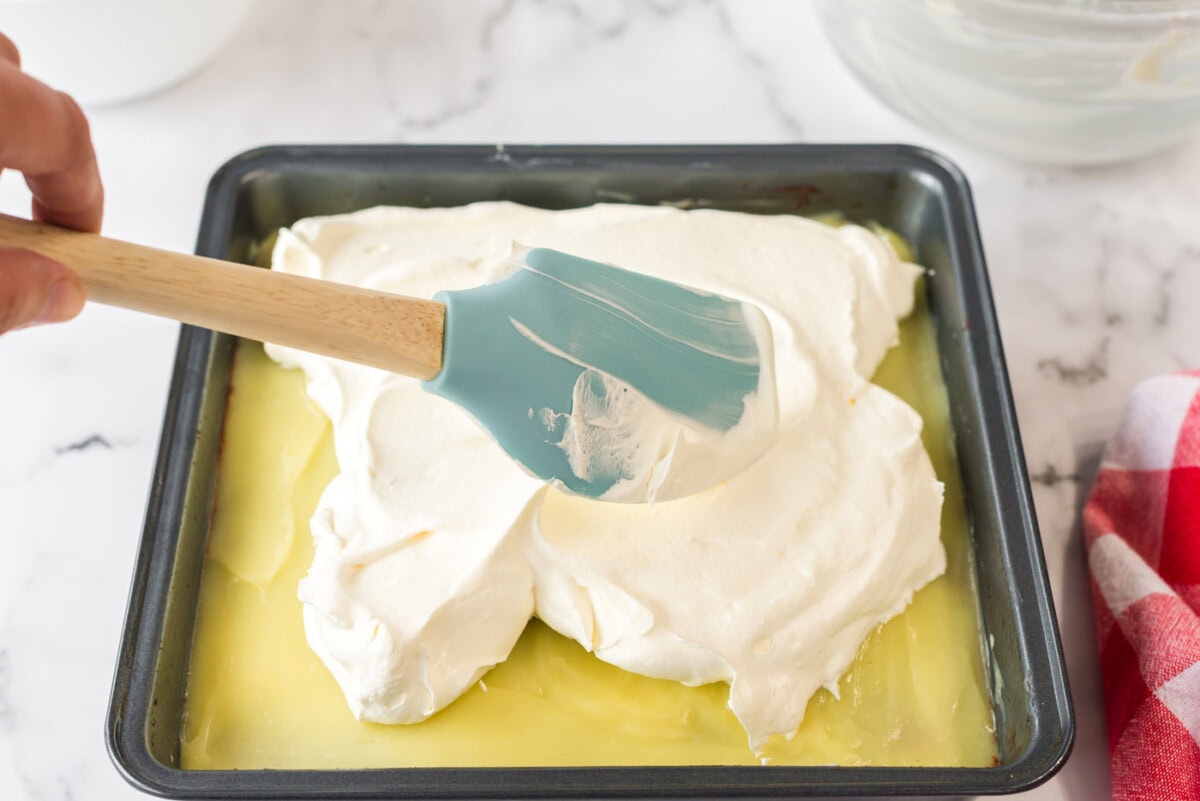Cool whip being spread over the vanilla pudding layer