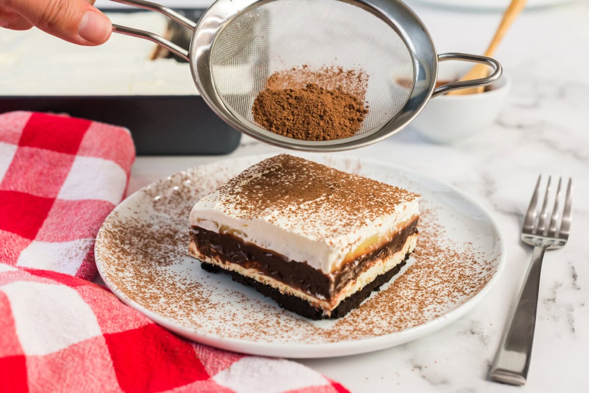 Cocoa powder being sifted on top of a slice of Sex in a Pan