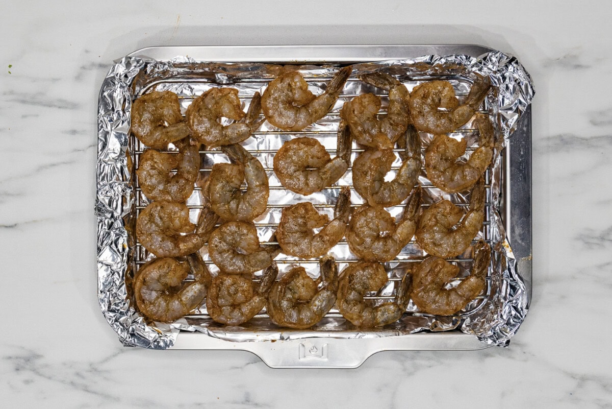 seasoned shrimp on a foil lined baking sheet with a wire rack