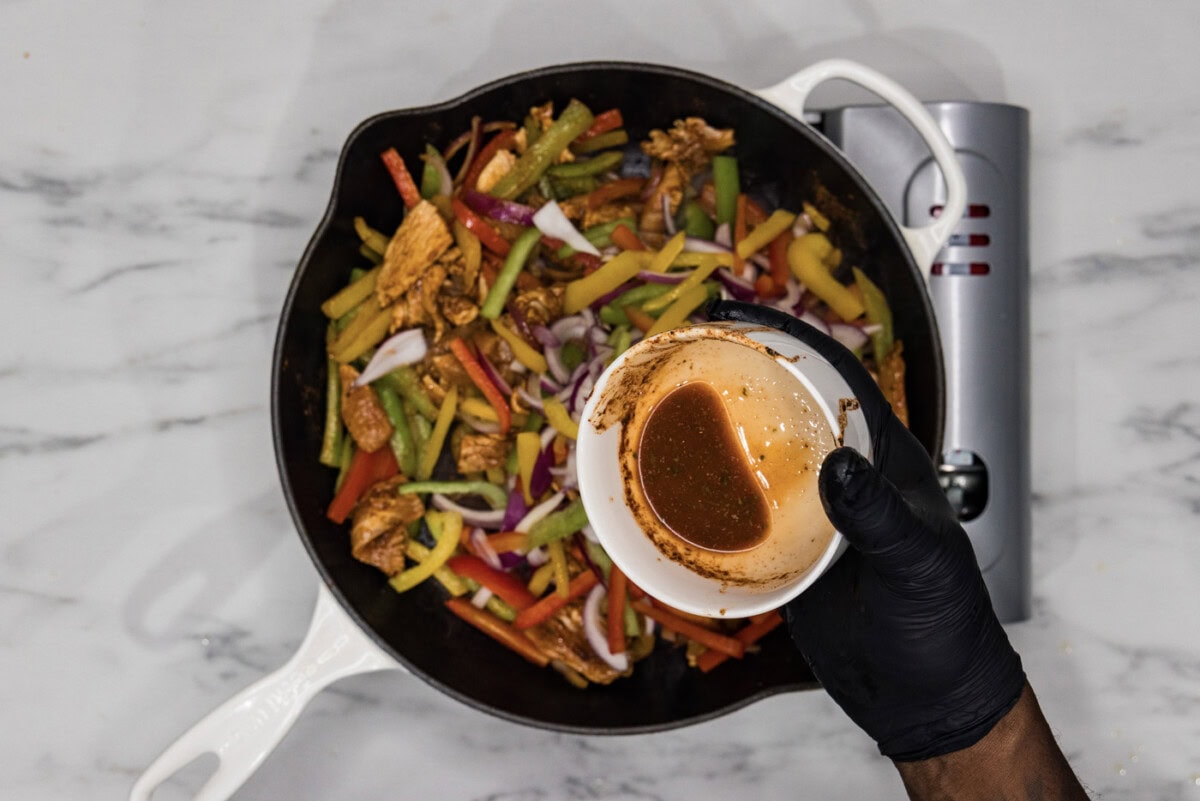 pouring remaining marinade into skillet with chicken fajitas