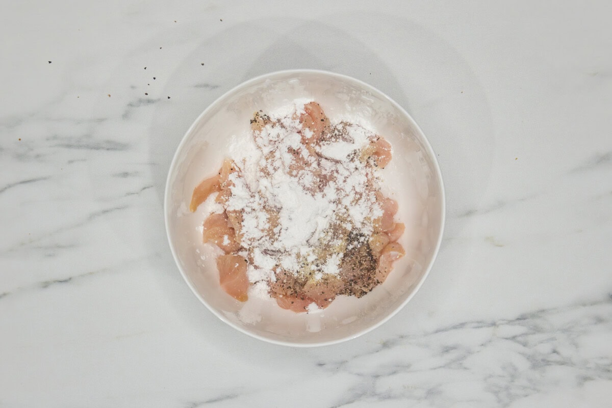 raw chicken pieces in a bowl with cornstarch and seasonings