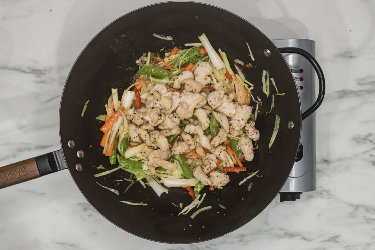 cooked chicken pieces added to wok with stir fried veggies