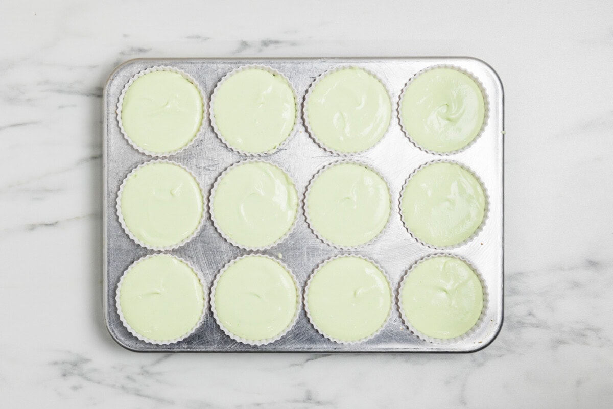 overhead photo of cheesecake mixture in silicone baking cups inside a muffin pan