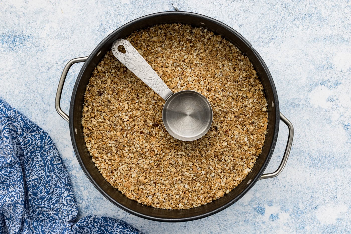 measuring cup pressing down almond graham cracker crust in a pan