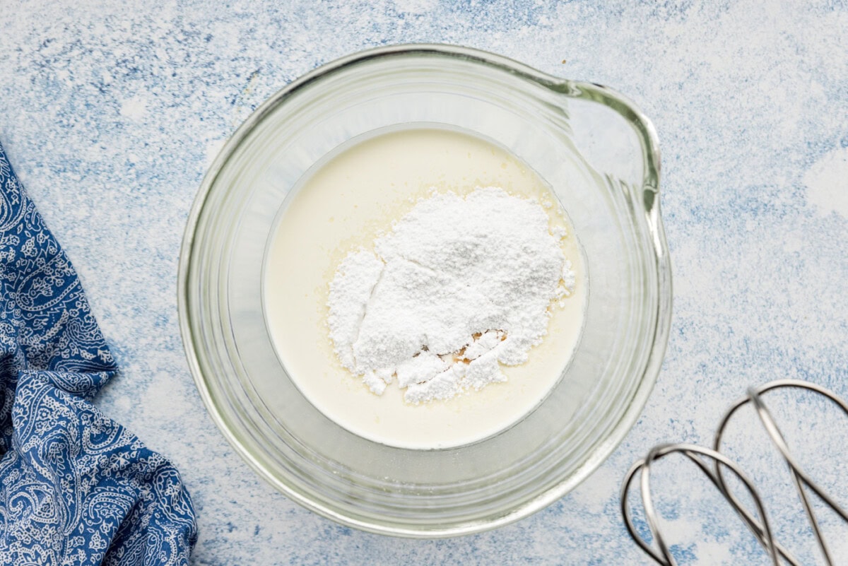 powdered sugar and vanilla extract added to heavy whipping cream in a bowl