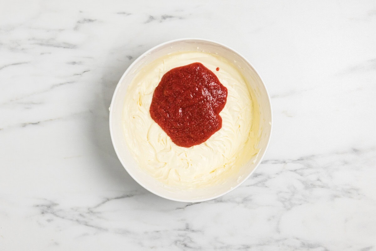 strawberry compote added to cheesecake batter in a bowl