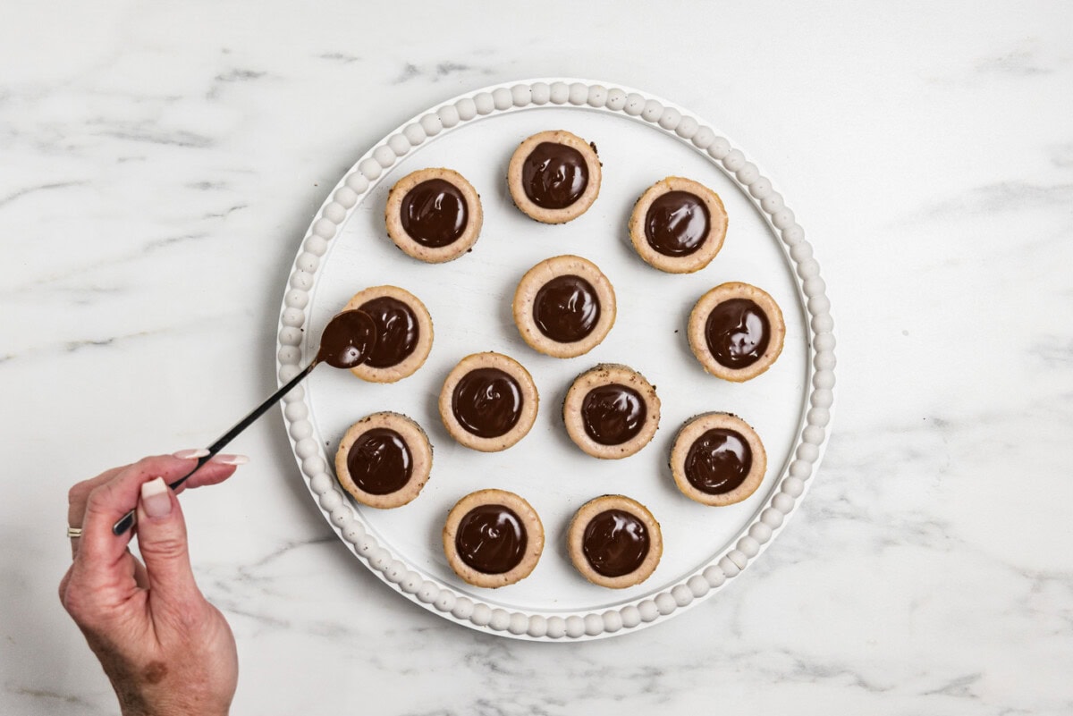 spooning chocolate ganache over mini strawberry cheesecakes