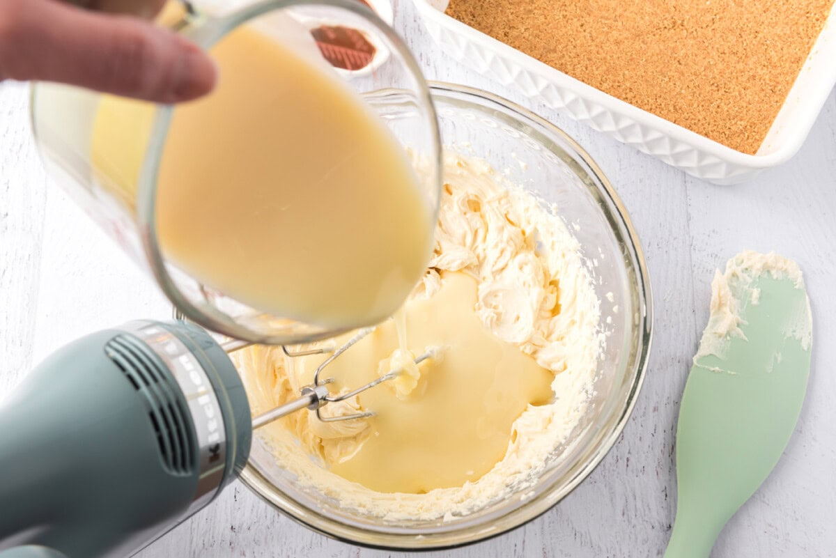 pouring sweetened condensed milk into mascarpone cheese mixture with a mixer