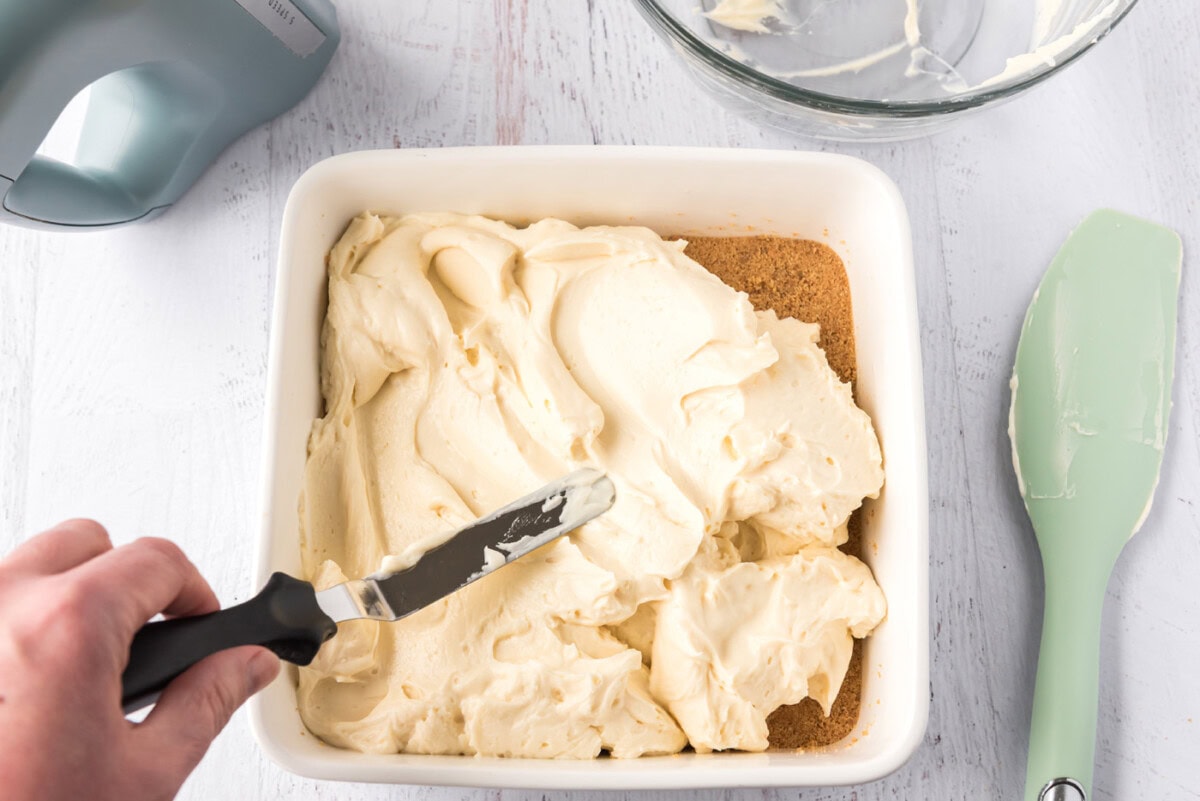 spreading mascarpone cheesecake over graham cracker crust in a pan