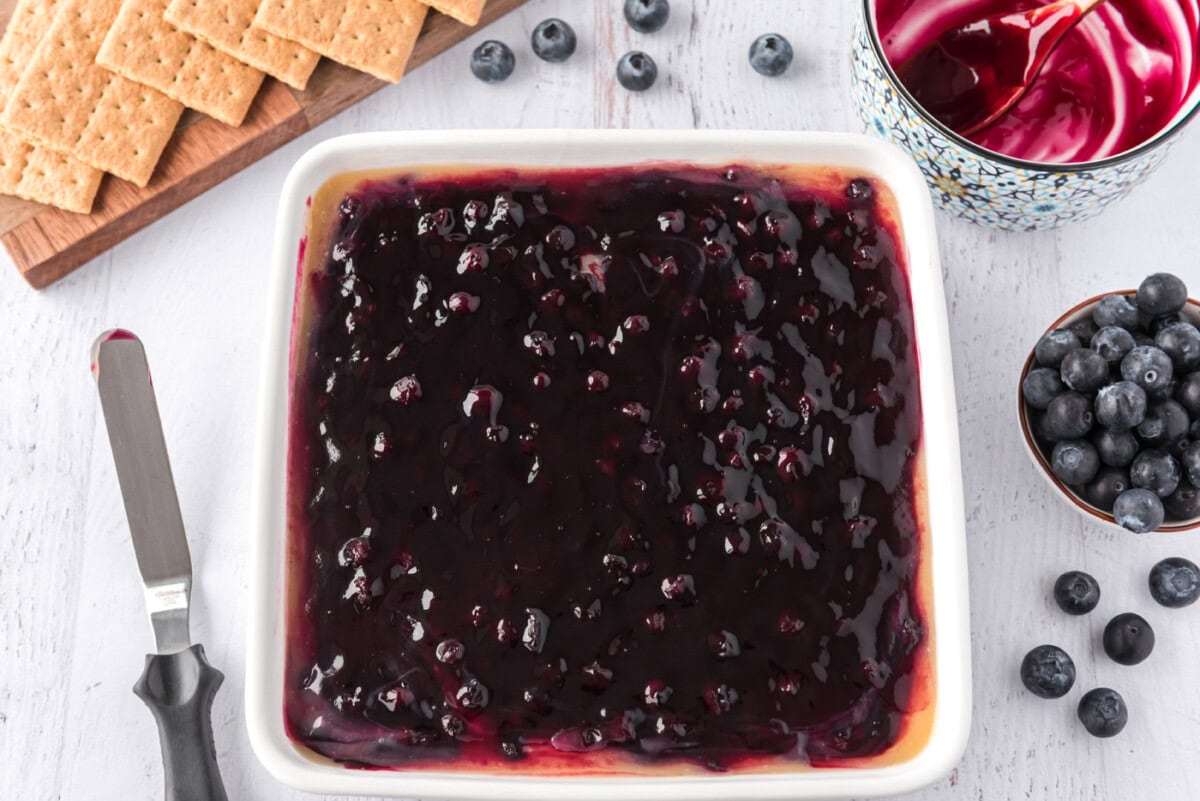 blueberry pie filling on top of cheesecake in a pan