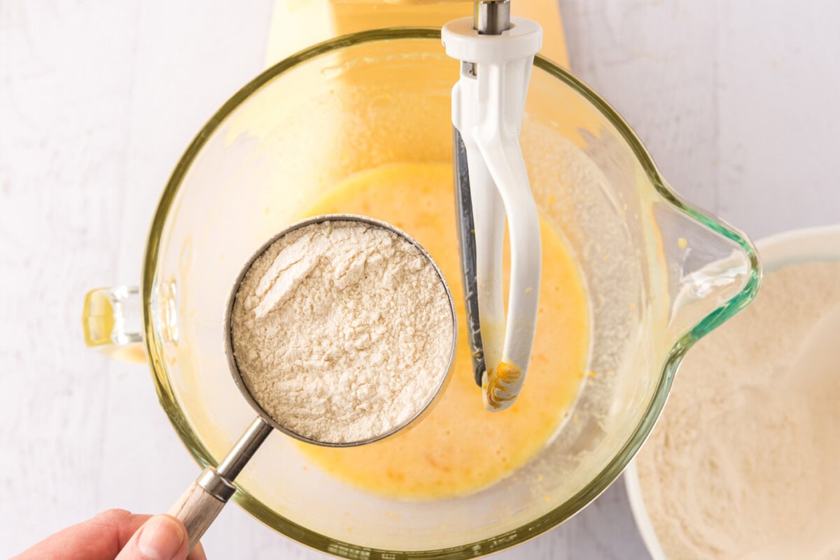 cup of flour over bowl of orange cupcake batter
