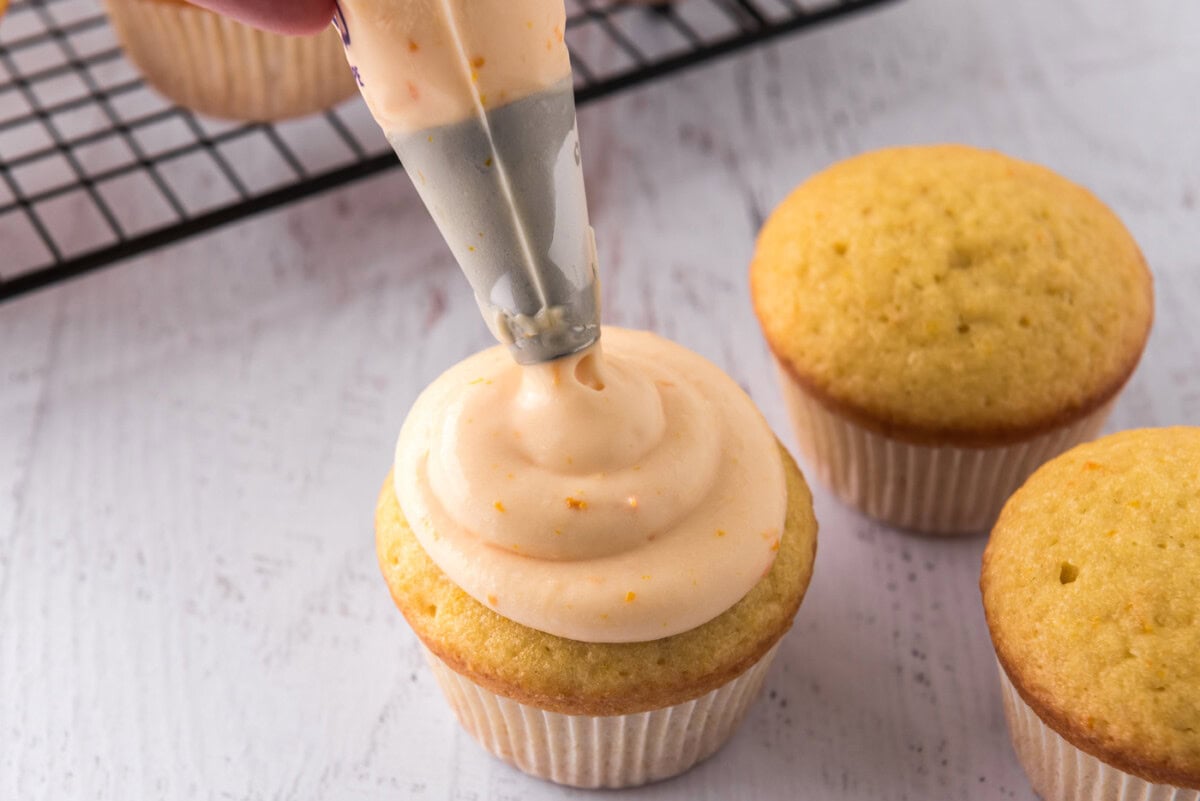 piping orange creamsicle frosting onto cupcakes