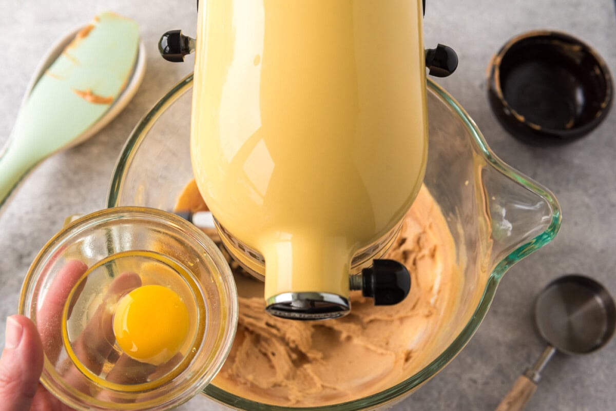 Adding eggs to a mixer bowl with peanut butter and cream cheese mixture