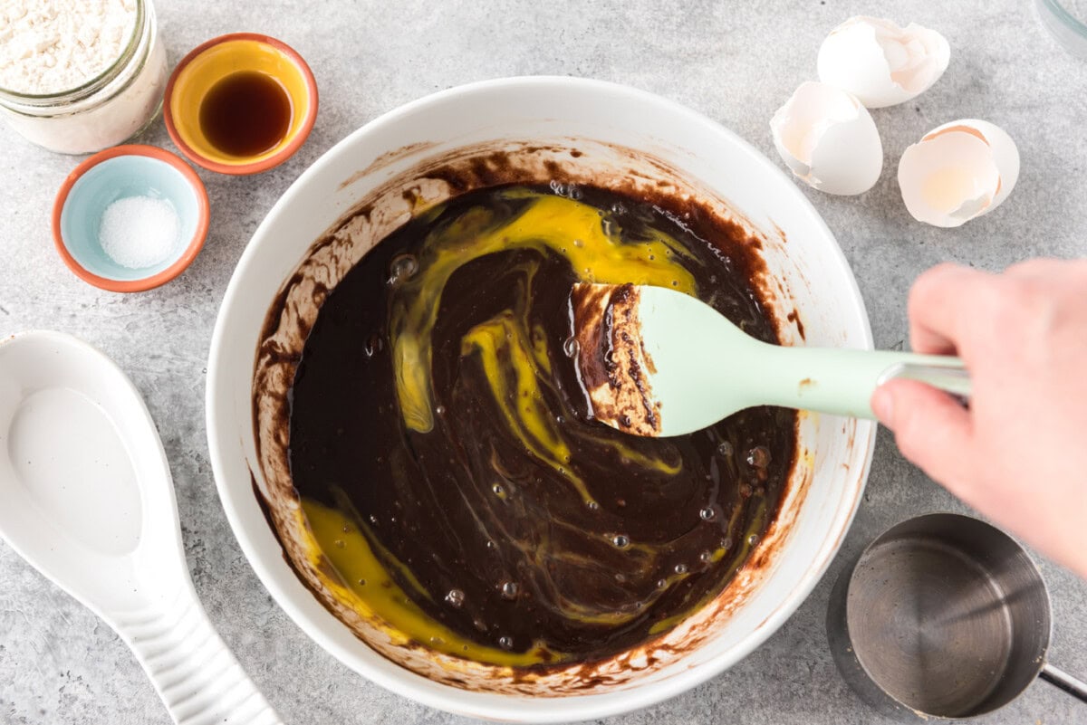 rubber spatula stirring egg into brownie batter in a bowl