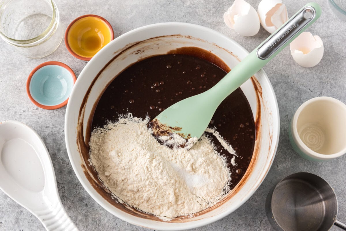 dry ingredients added to a bowl of brownie batter with a rubber spatula