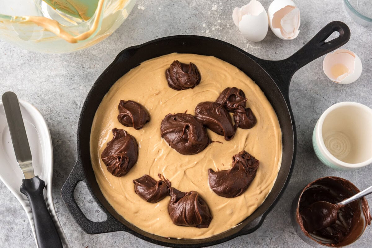 dollops of brownie batter on top of peanut butter mixture in a cast iron skillet