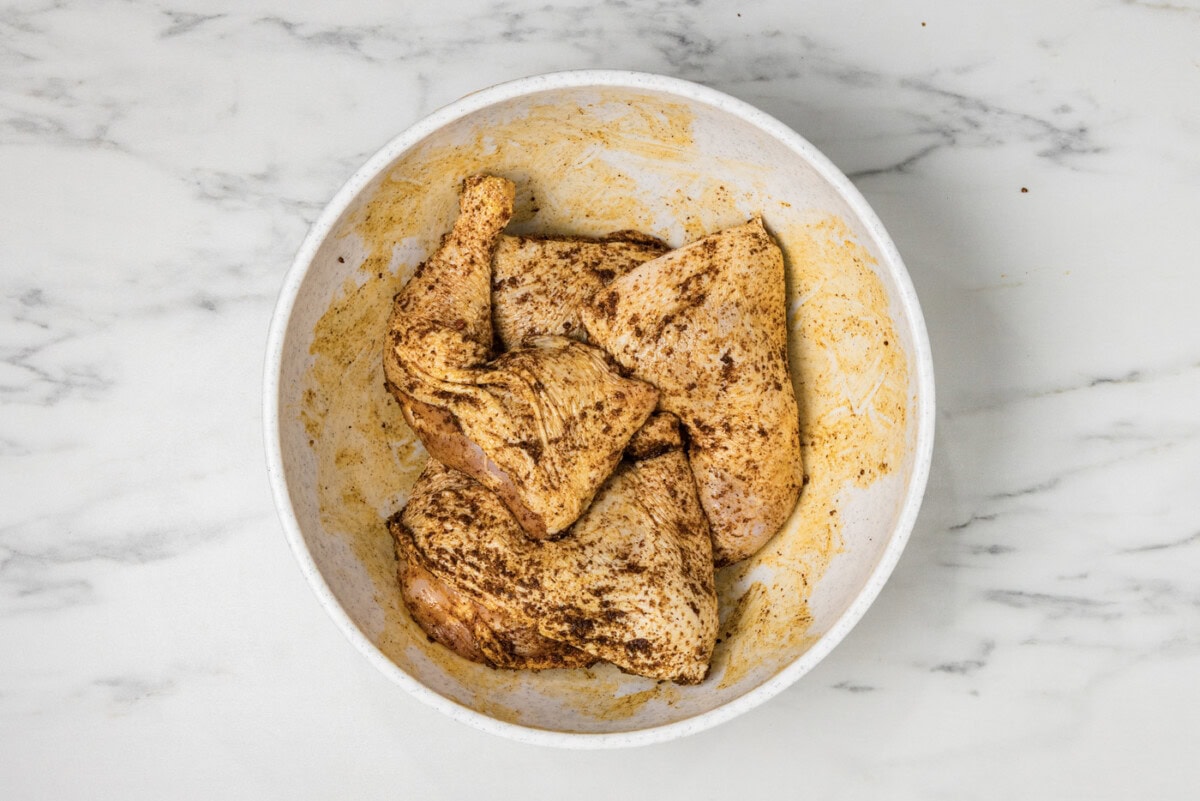 raw chicken quarters in a bowl with wet rub