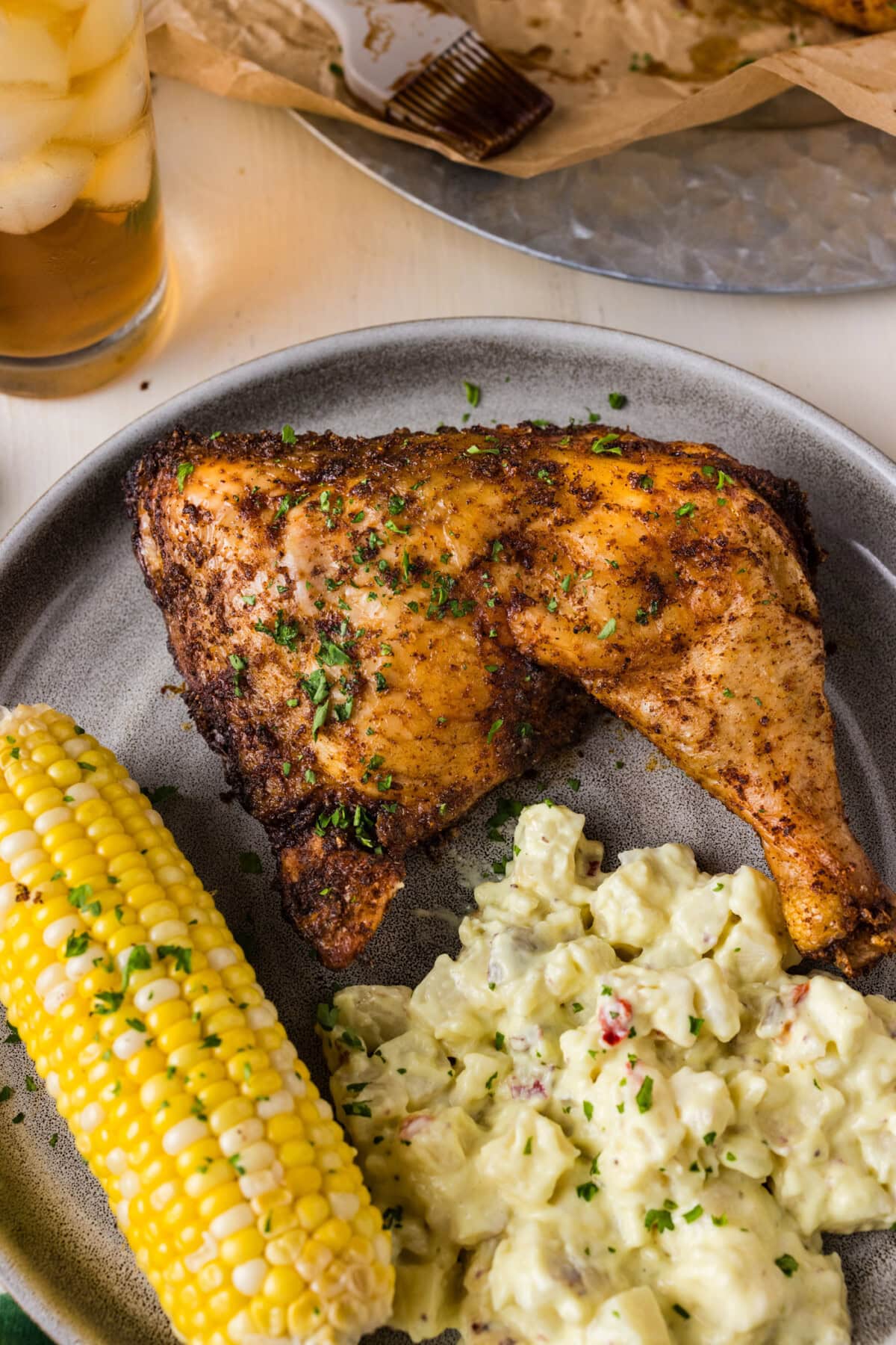 Close up photo of a Smoked Chicken Quarter on a plate with potato salad and corn on the cob