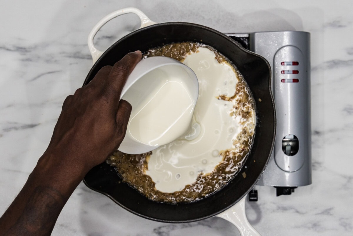 pouring heavy cream into skillet with shallots and garlic
