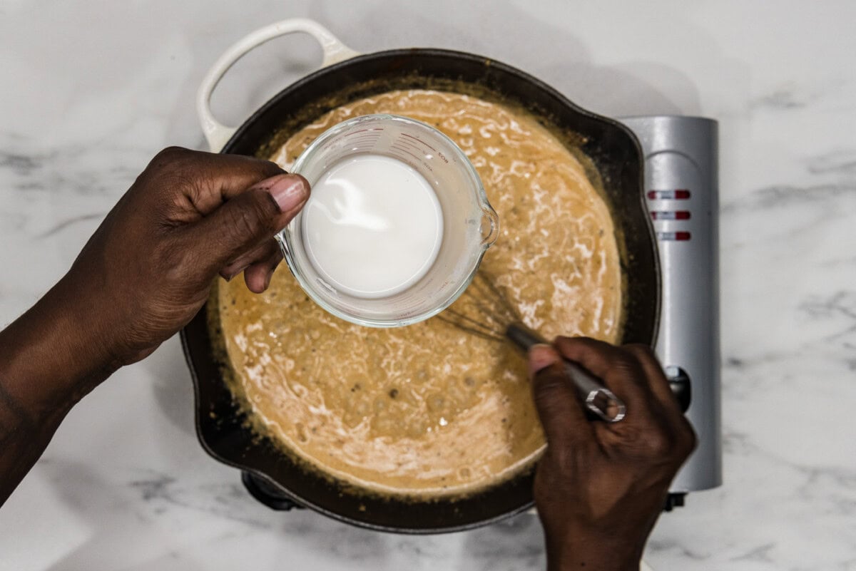 whisking cornstarch slurry into tuscan chicken sauce in a skillet