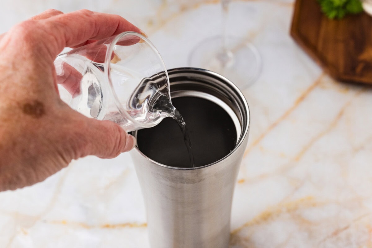 pouring cucumber vodka into a cocktail shaker