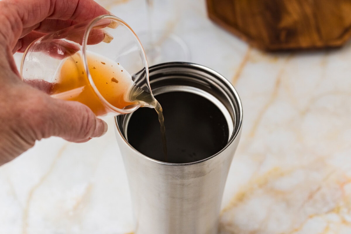 pouring olive juice into a cocktail shaker