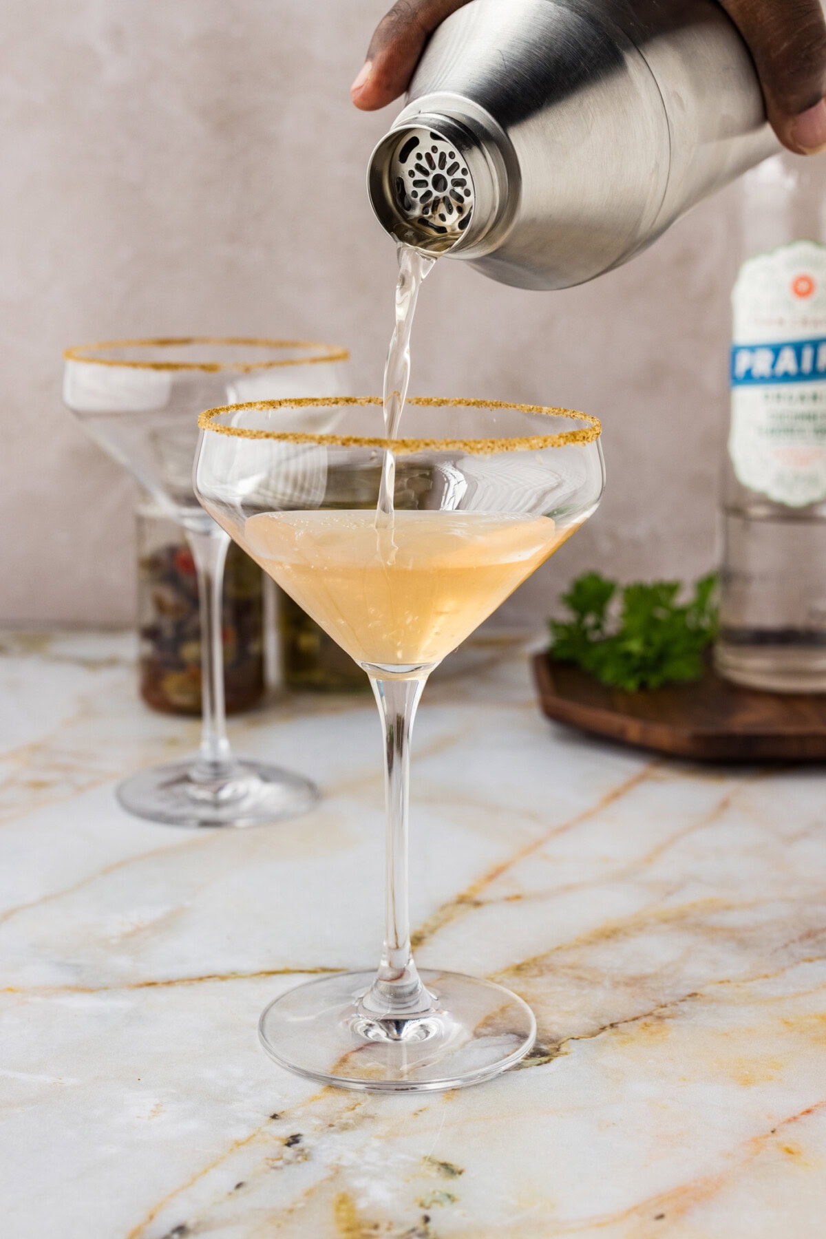 pouring dirty greek martini from a cocktail shaker into a glass