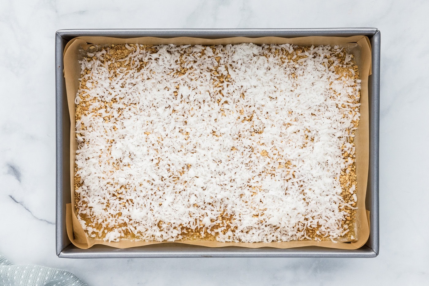 shredded coconut sprinkled over graham crumbs and melted butter in a baking pan