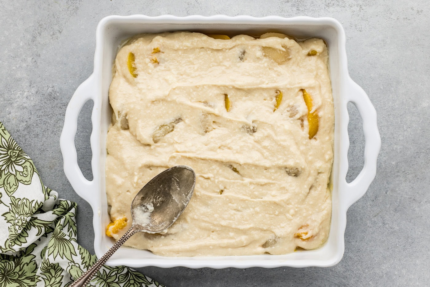 spoon spreading out cobbler batter on top of peaches and pears in a baking dish